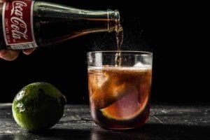 A person is pouring coca cola into a glass of rum, one of the best way to enjoy rum